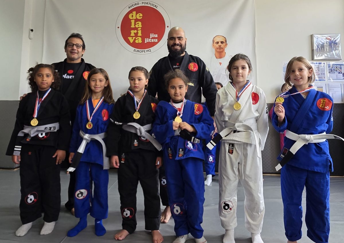 Alunas do Kids III com medalhas e os professores, em frente ao logótipo da Escola Delariva Aveiro